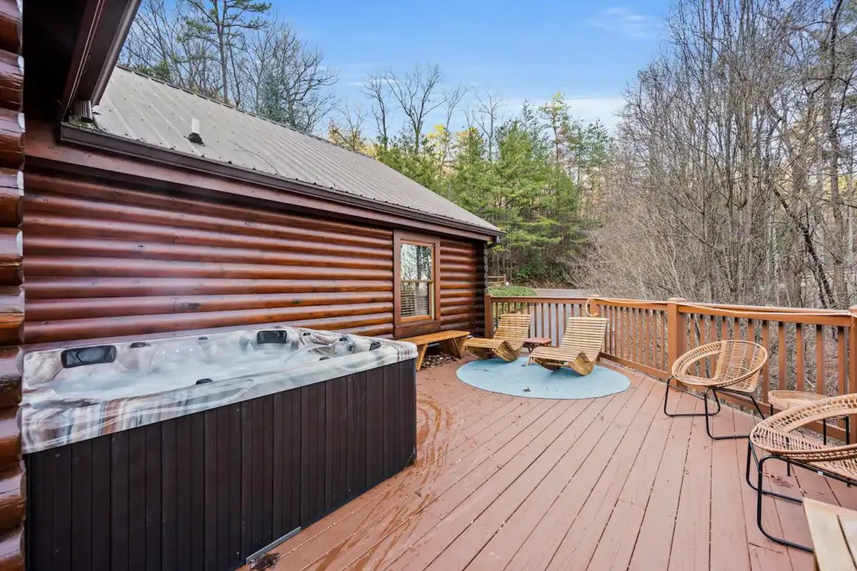 An exterior shot showcasing a hot tub on a wooden deck surrounded by tall trees, with lounge chairs and ample space for groups to gather. The hot tub is the focal point, offering a perfect spot for relaxing and socializing under the stars after an action-packed day.