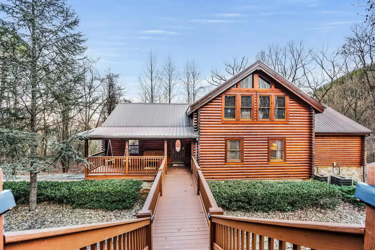 A charming log cabin with a welcoming front porch, wooden walkway, and surrounded by lush trees. The inviting porch hints at outdoor gatherings and serves as a gateway to nature trails nearby, echoing the adventurous spirit of the Smoky Mountains.