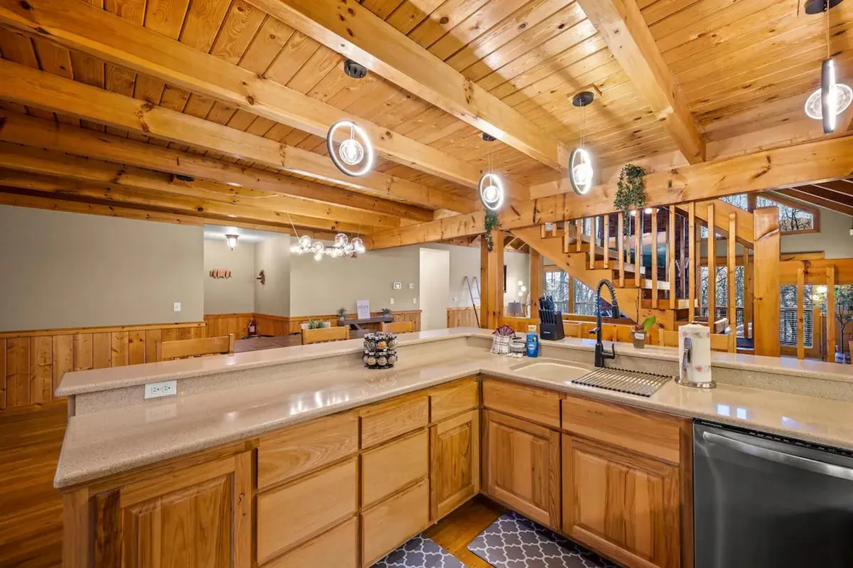 Here, the kitchen island is front and center, complemented by wooden beams, stainless steel appliances, and inviting pendant lighting. The space feels open and perfect for group meal prep or casual breakfasts, with plenty of workspace and an atmosphere that encourages gathering.