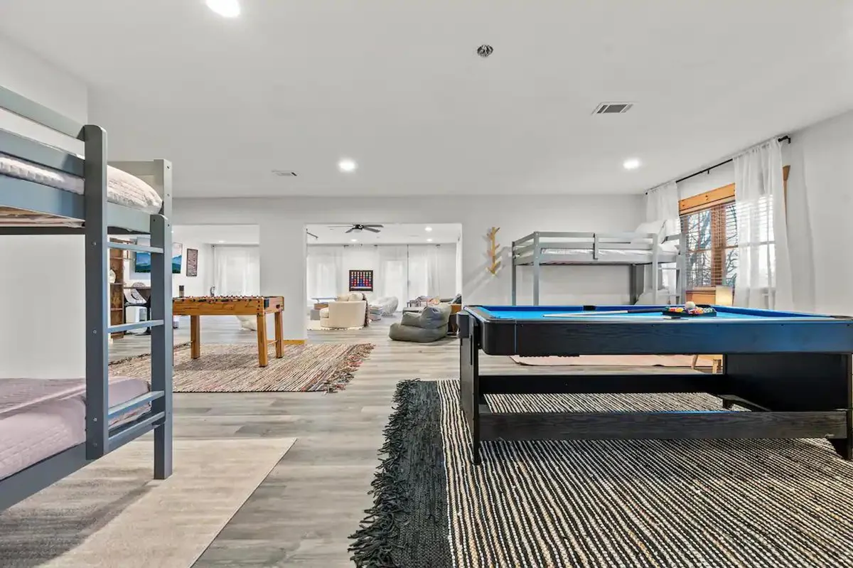 A bright, fun-filled game room featuring bunk beds, a pool table, foosball table, and large windows that bring in natural light. The space is lively and ideal for group activities, relaxation, and bonding after a day of exploration.