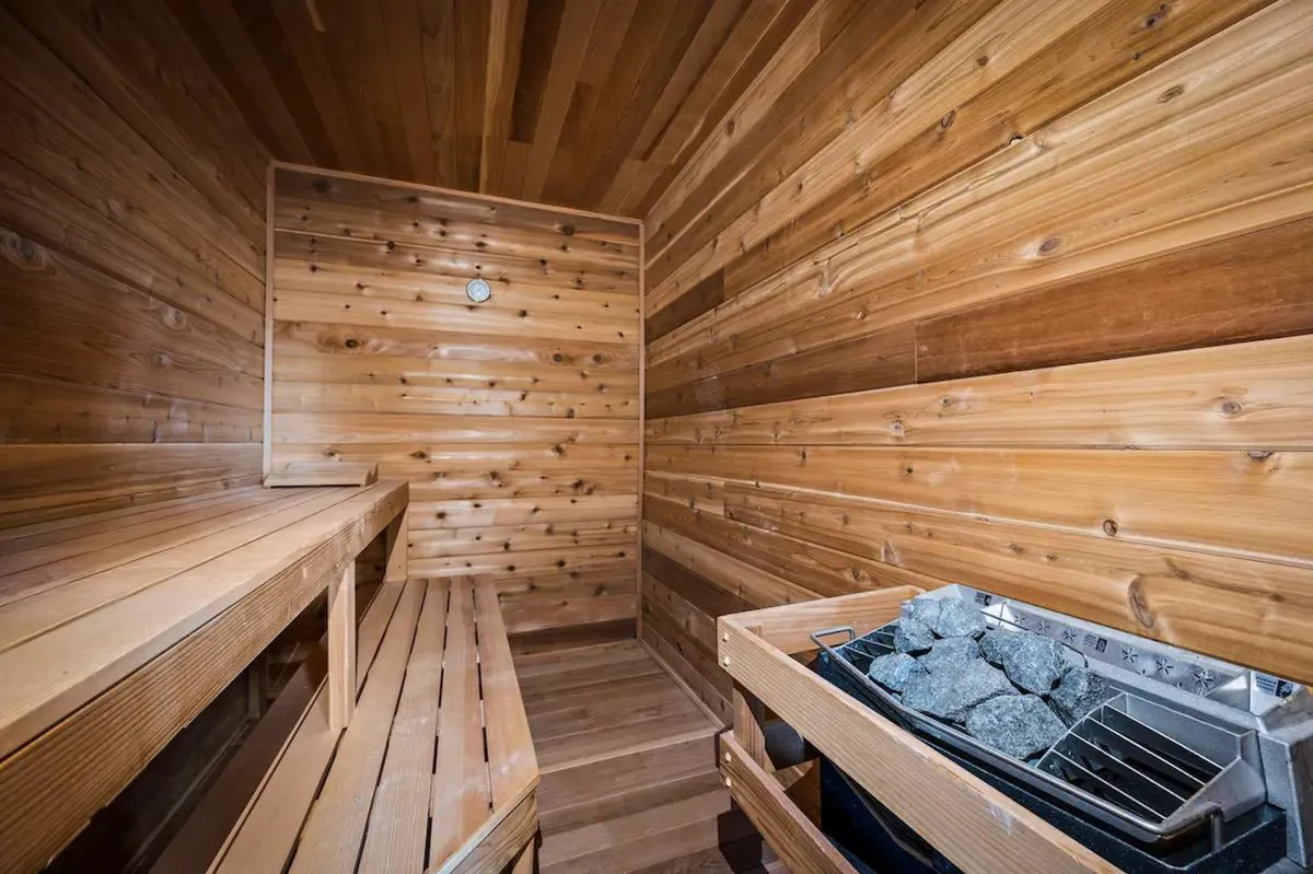 A beautifully crafted sauna interior featuring warm wooden benches, a stone heater radiating gentle heat, and wood-paneled walls. The inviting space is softly lit, creating a tranquil atmosphere perfect for wellness routines and relaxation.